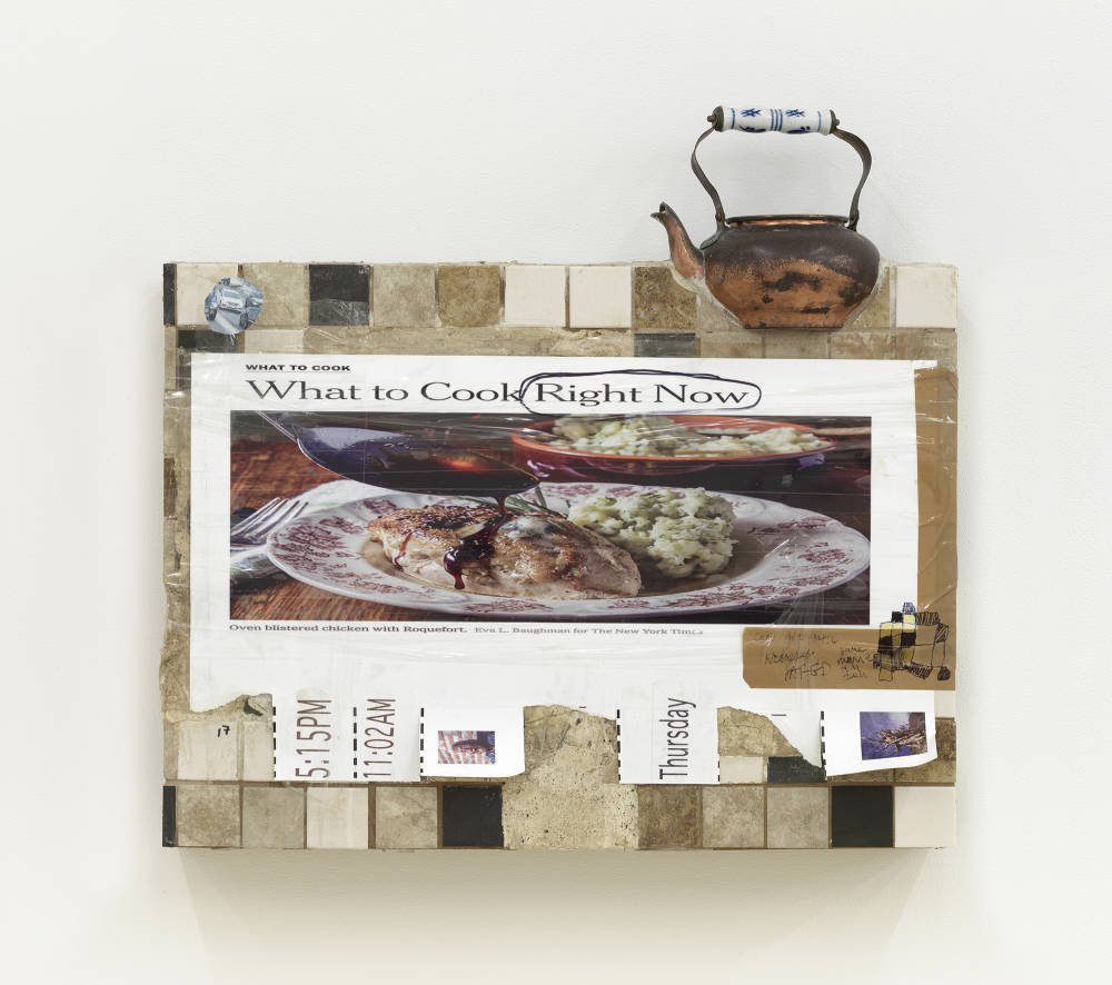 On a white wall, a rectangular sculpture jutting out from the wall with a printed New York Times recipe. The image is framed with packing tape and many kitchen tiles. At the top right edge a vintage tea kettle jutting out from the object. 
