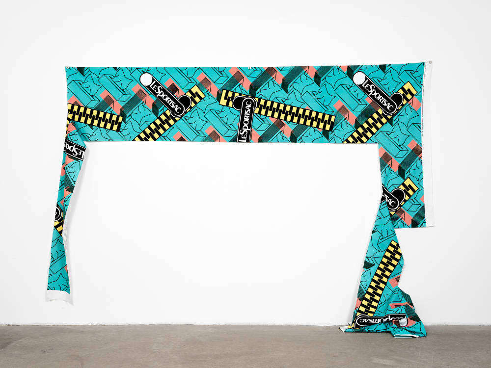 A custom designed and printed fabric scrap, attached to the wall horizontally, with a cut piece of fabric draping down and touching the ground.