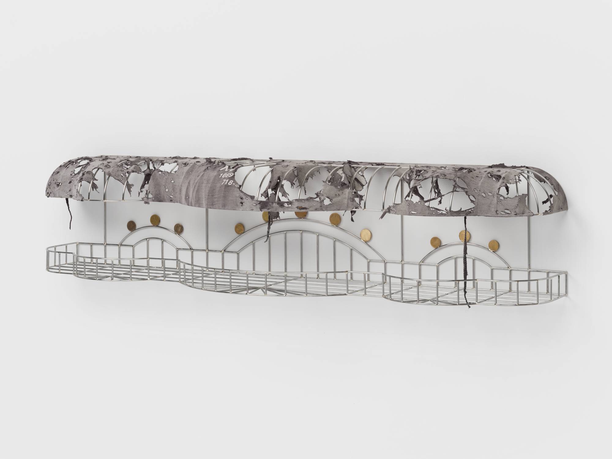 Angle view of a cage-like chrome sculpture, wrapped with a tattered grey t-shirt to resemble an awning, and embellished with soldered on gold-colored coins.