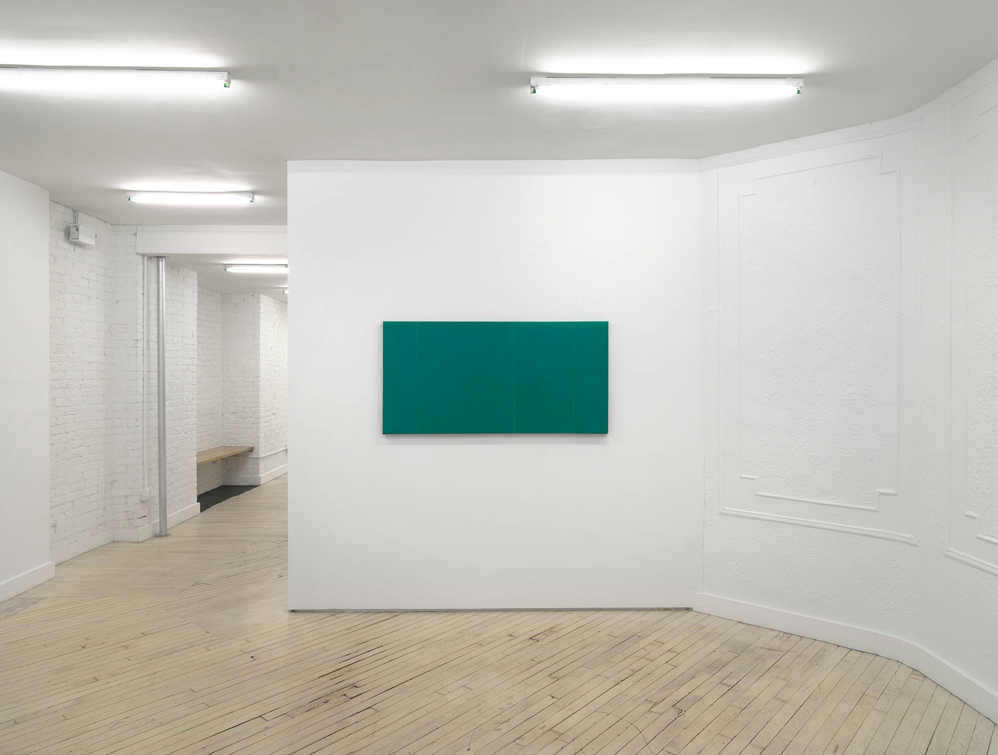 In a gallery space, a horizontal muted green painting hangs in the center of a wall.