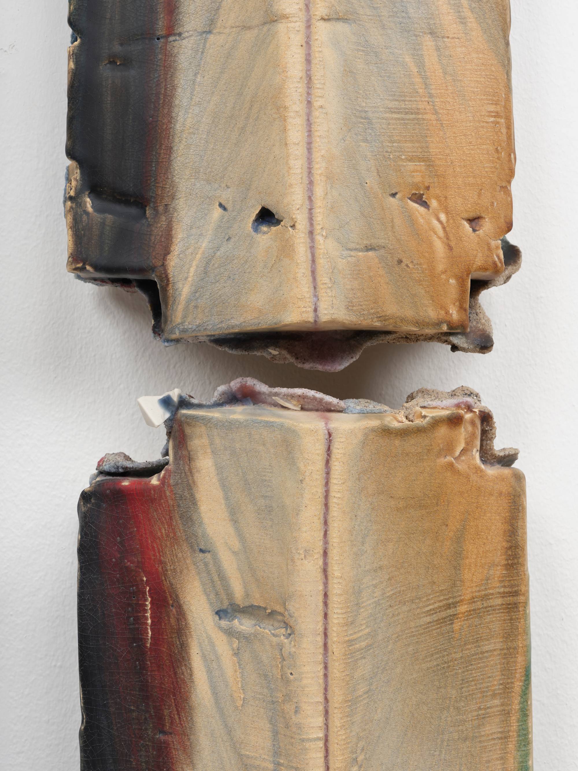 Detail of four individual cross shaped ceramic sculptures are mounted to a white wall in a square orientation to form the shape of a pound sign (#). They are glazed in hues of aqua, red, and yellow.