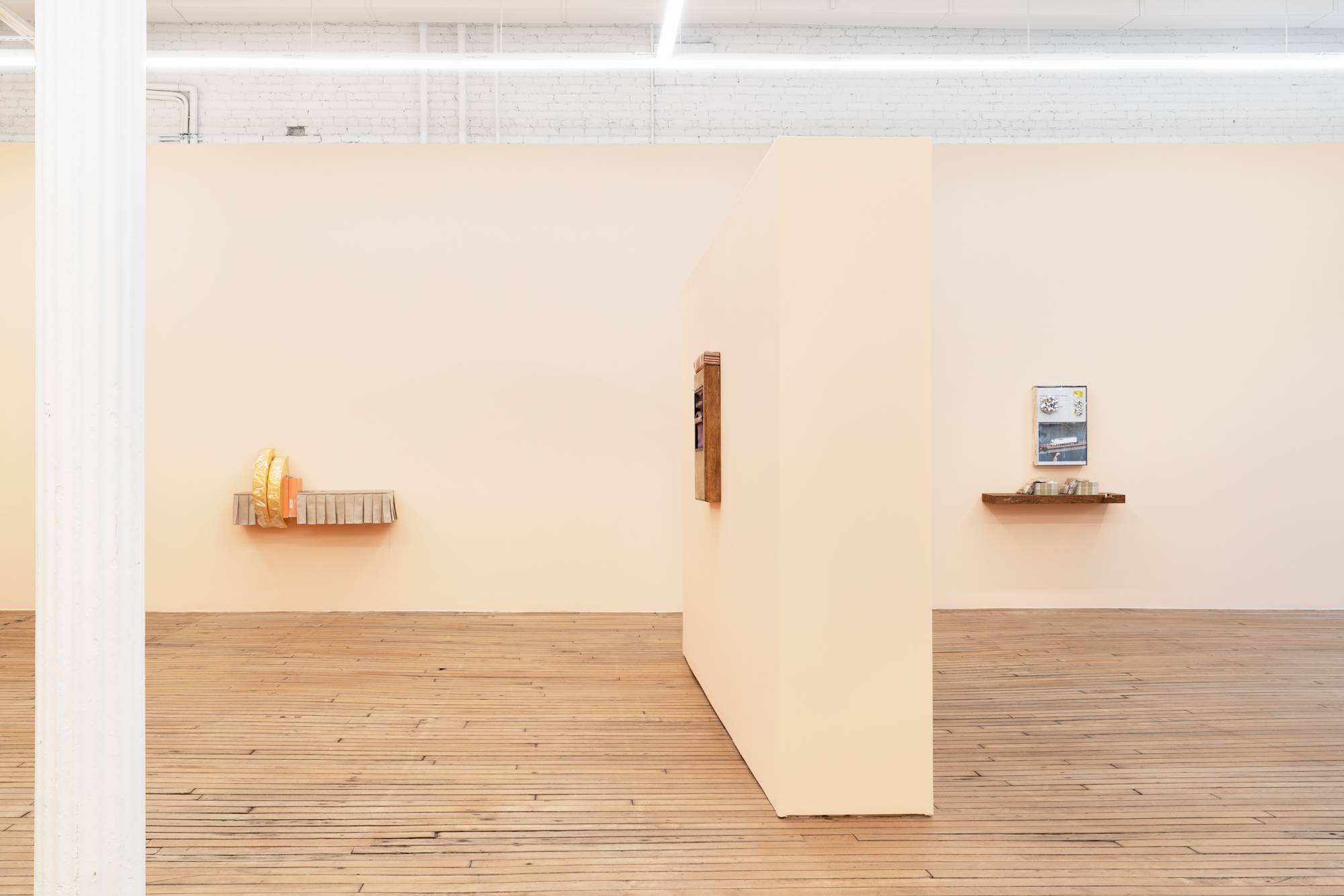 Interior view of art gallery with wood floors and peach colored walls. Various sculptures hang on the walls.