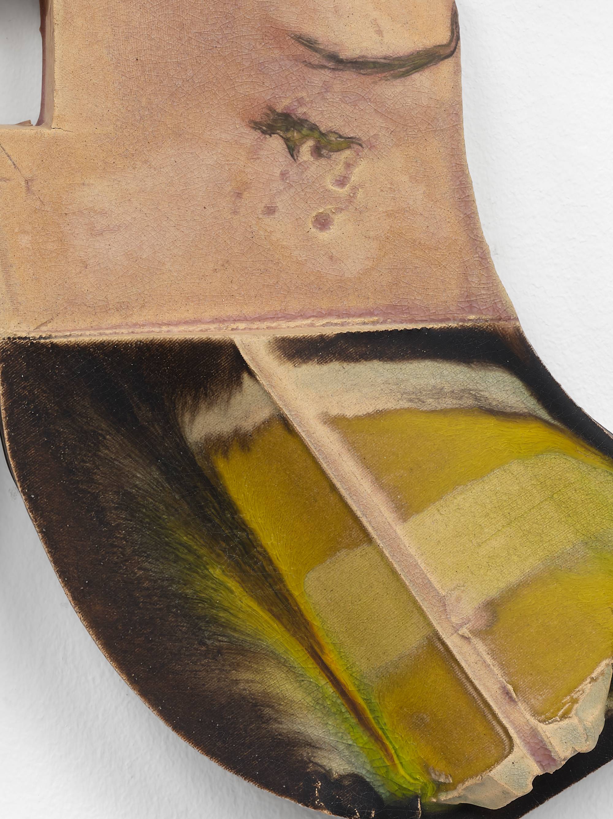 Detail of two ceramic sculptures hanging on a wall mirroring each other. The two pieces resemble the letter "J", one forwards, one backwards. A spine runs diagonally down each bottom swoop, striped with yellow and green glaze, against a background of dark brown glaze.