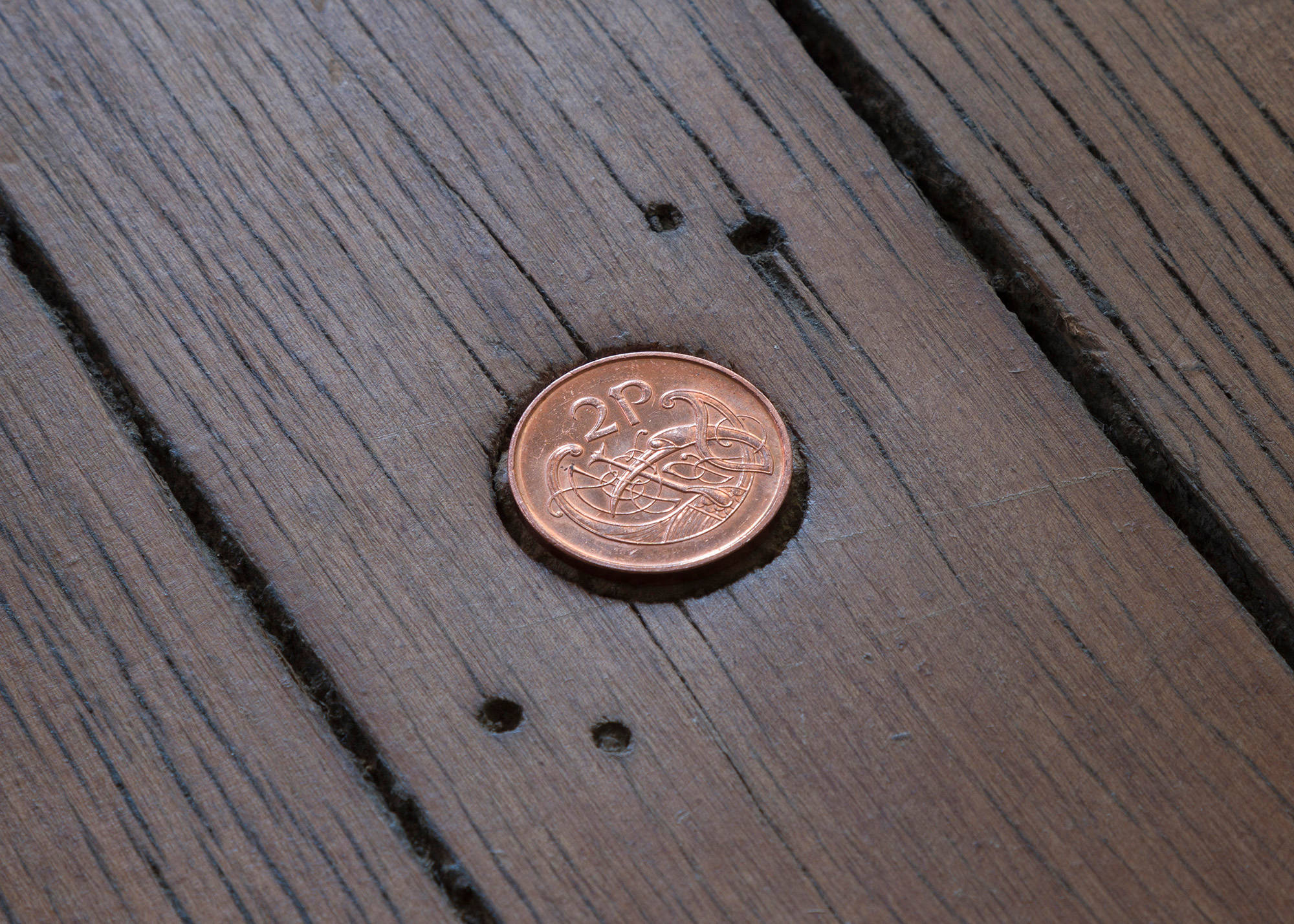 A close up image of an irish two pence coin inlaid into a wood floor.