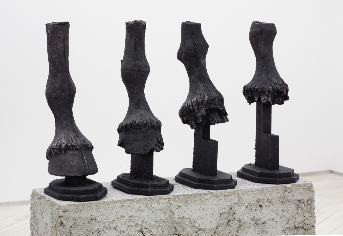 Four cast iron horse hooves in a row on top of a concrete base. 