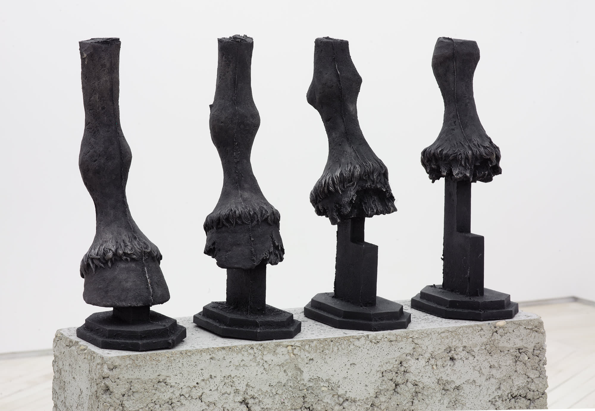 Four cast iron horse hooves in a row on top of a concrete base.