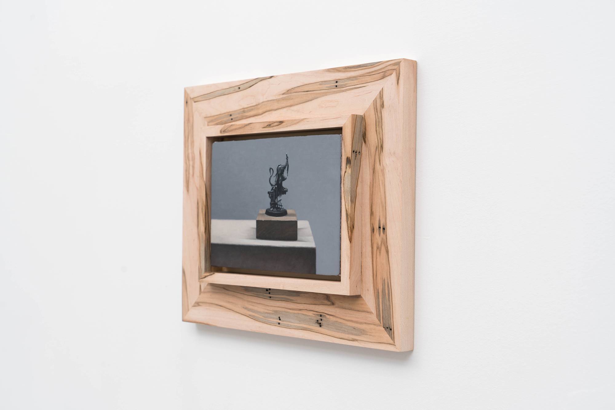 3/4 view of Ian Miyamura painting depicting an unpainted Warhammer figure sitting on a wood block against a grey background. The painting is mounted to a wood frame made by the artist.