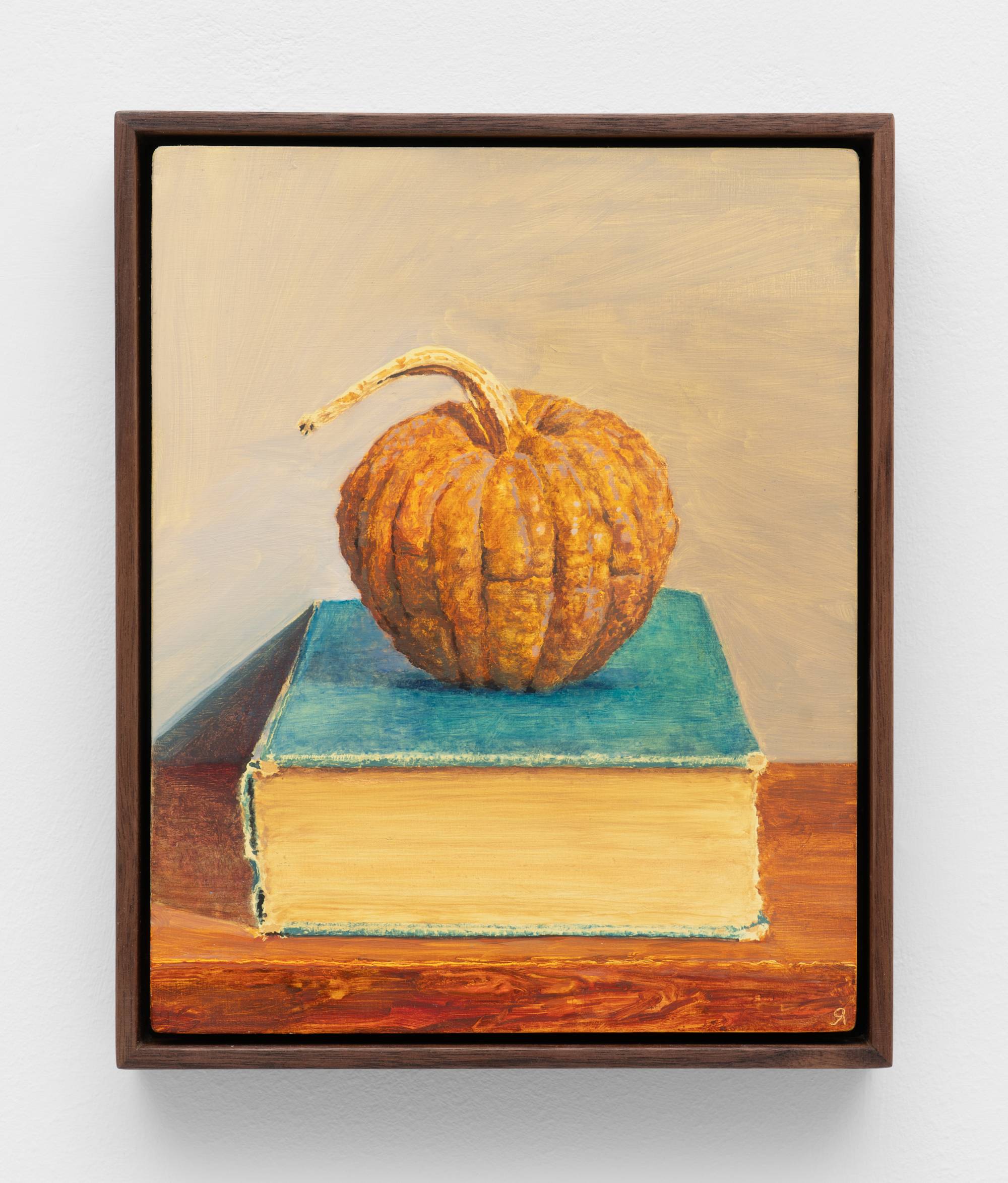 A small, dark wood framed painting of a squash sitting atop a thick and weathered blue book.