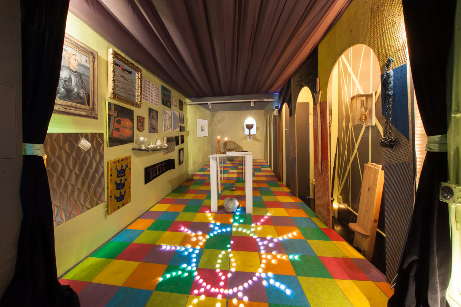 Image of a dimly lit room with a colorful tiled floor. A lighting design is projected onto the floor in the shape of a circle with emanating rays and a symbol in the middle. Paintings line the left wall, and arches line the right wall, with shallow depths. Dark Curtains frame the image of the room.