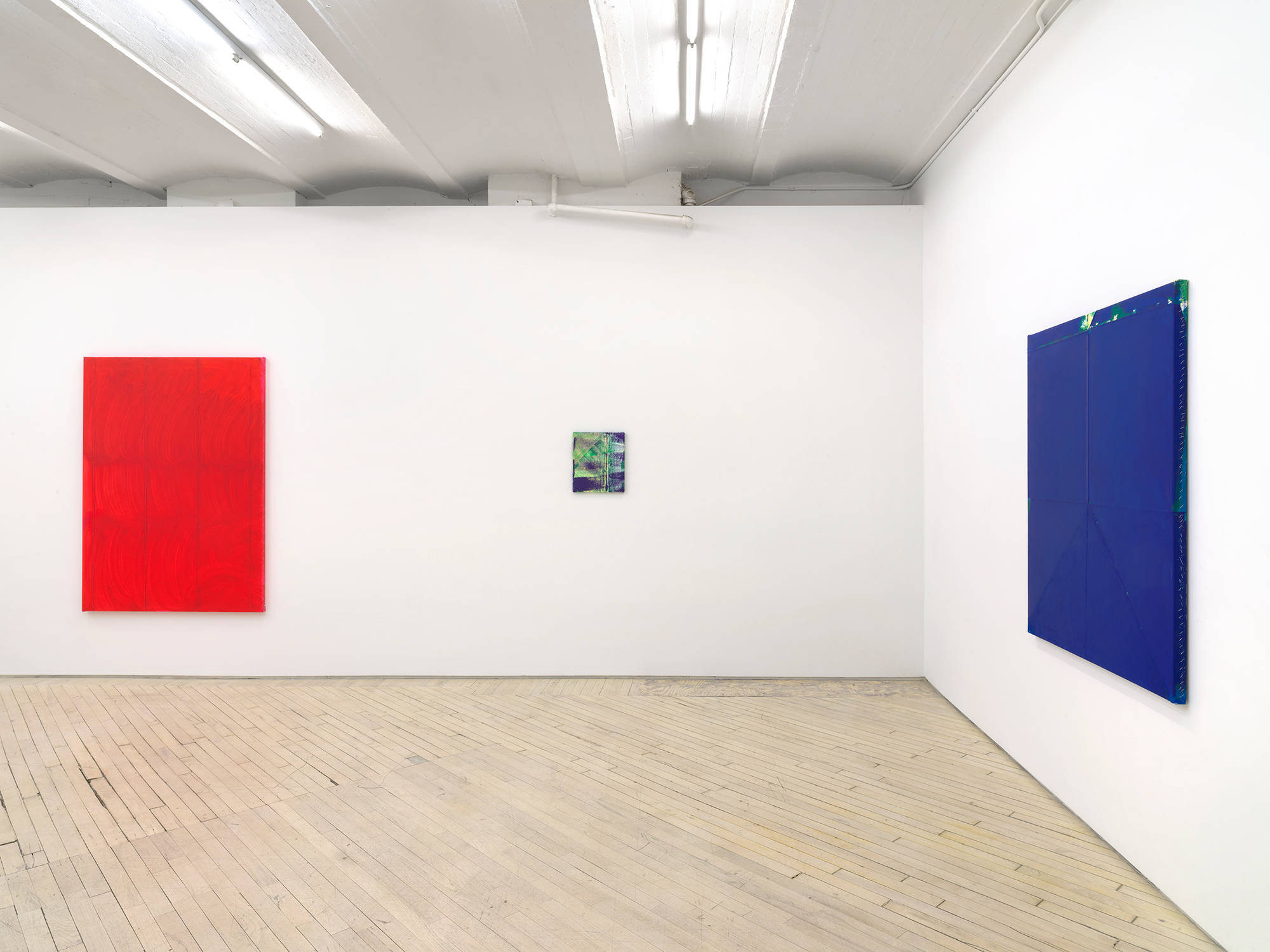 In a gallery space, a monochromatic red painting with a brushy surface. To its right is a small brushy green and purple painting. On the right wall a large blue monochromatic painting