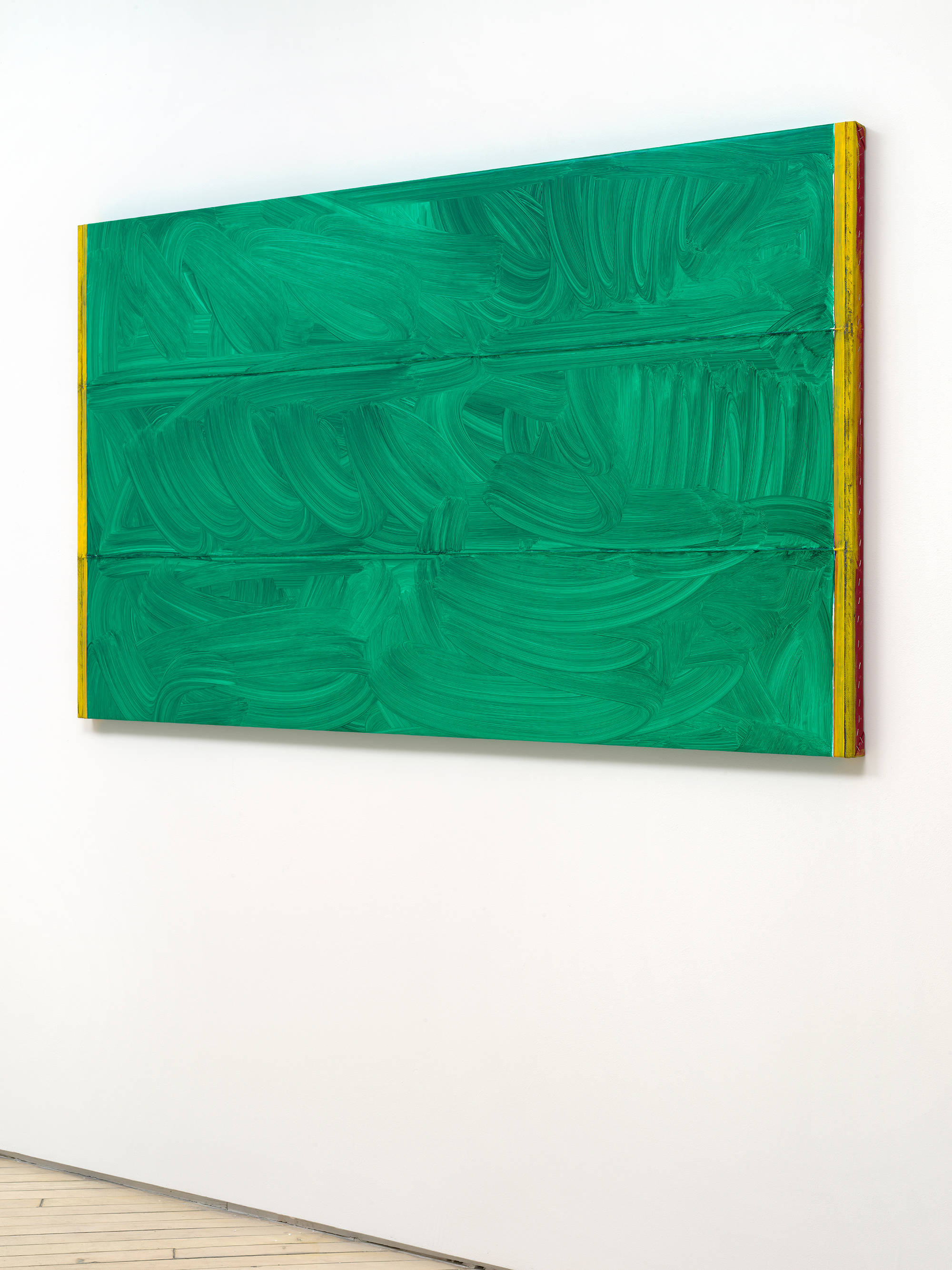 A side view of a horizontal abstract painting with a brushy green surface. On the left and right edges are yellow and red bands of color.