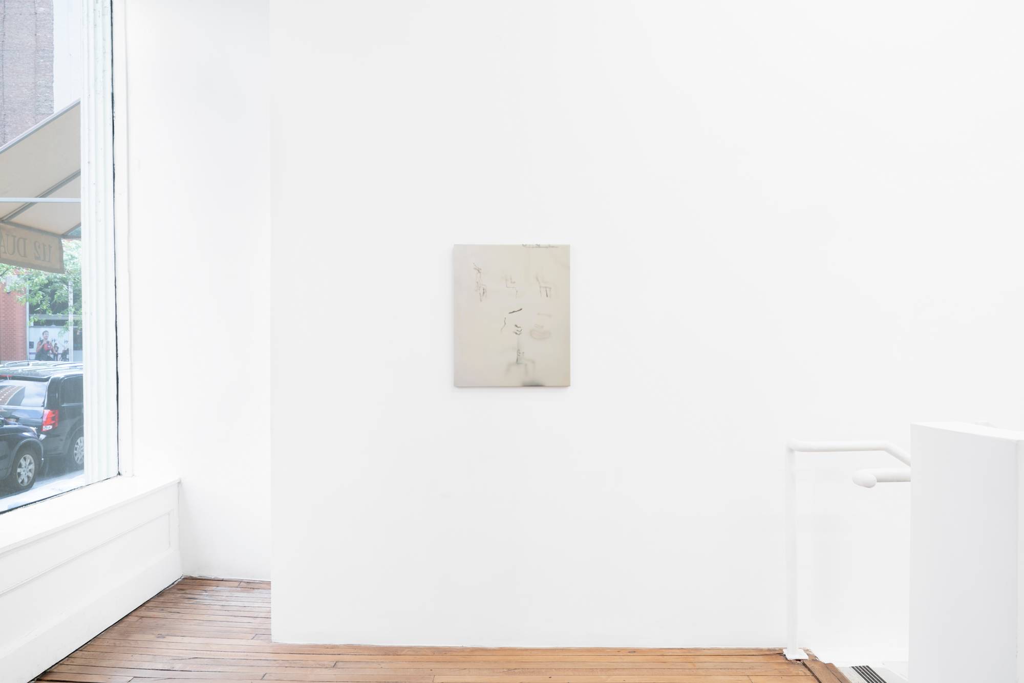 In a gallery space next to a large window and stairwell hangs a small abstract painting, rendered primarily in white depicting a series of airbrushed marks.