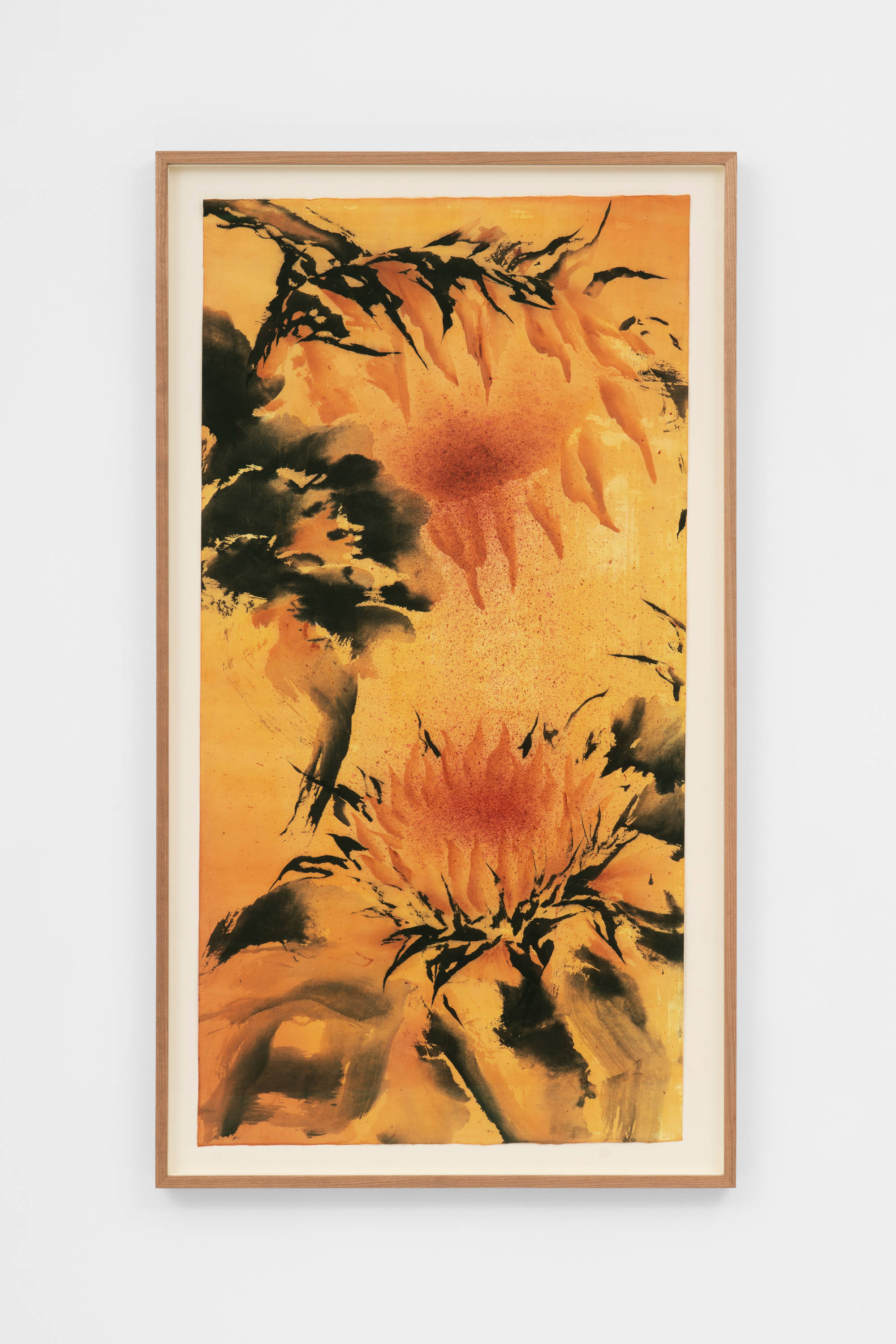 An ink painting of two orange-ochre sunflowers: one flower at the top left of the composition, and the other at the bottom right of the composition, with the heads of the flowers facing each other. Each flower is surrounded by black leaves and is set against a background of a similar coloration as its petals. The frame and the wall the work is mounted on is visible in the shot.