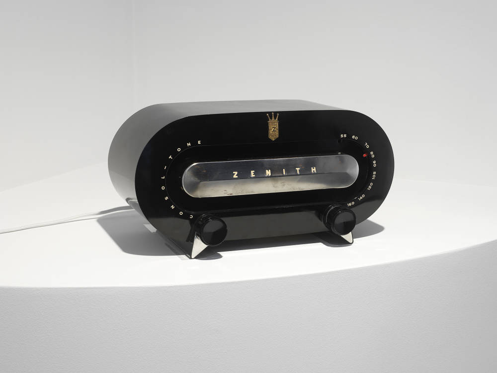 A black vintage radio with silver accents on top of a white shelf. 