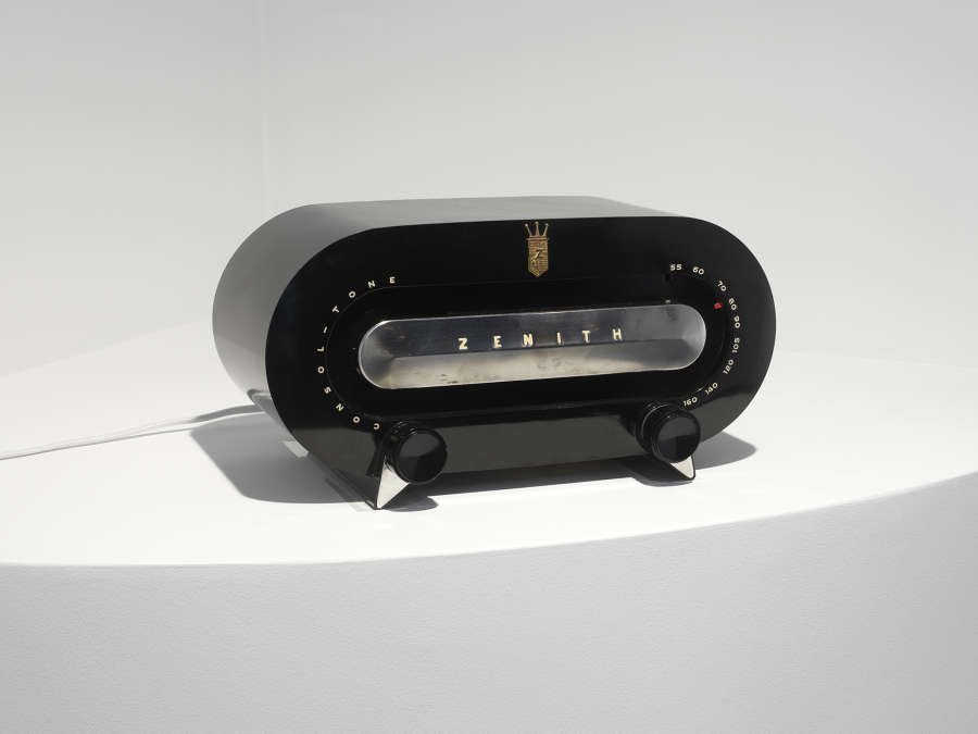 A black vintage radio with silver accents on top of a white shelf. 