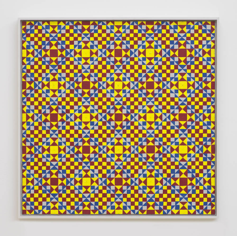 On a white wall a painting depicting a grid of crisscrossing lines generating many rectangles, triangles, circles. The dominant colors are hues of yellow, red, blue. The frame is painted gray.