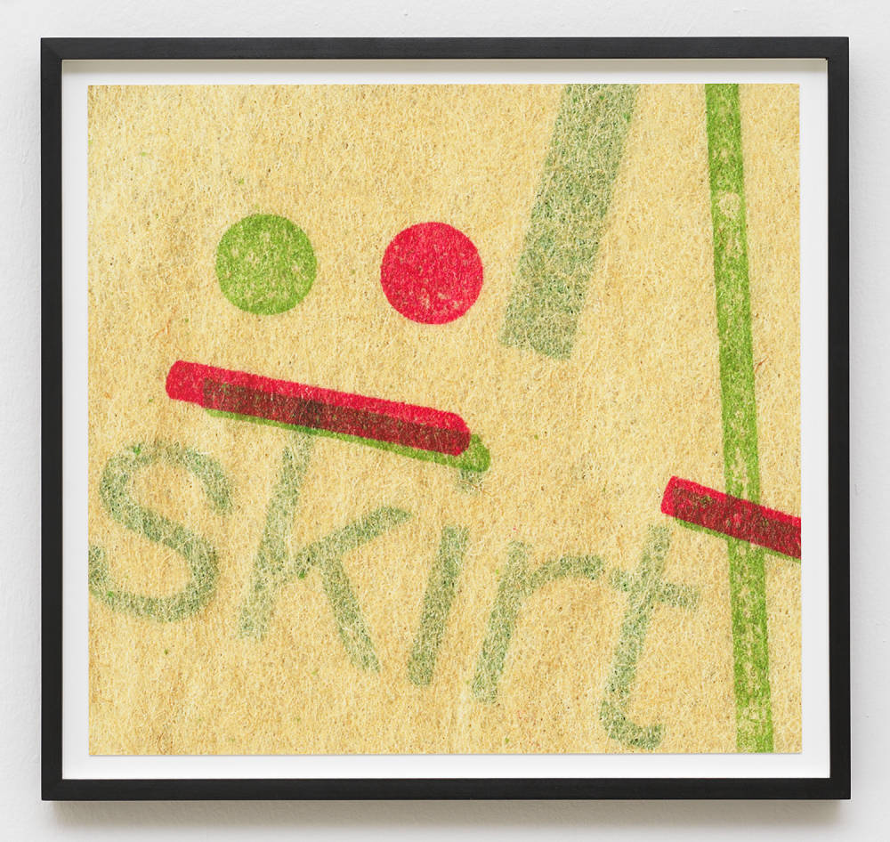 Image of a photograph in a black frame, the photograph depicts an up close look at a vintage sewing pattern. The pattern's paper is yellowed and coarse. The pattern is cropped and visible are a series of straight lines and two dots in green and red, faintly you can see the word "skirt."