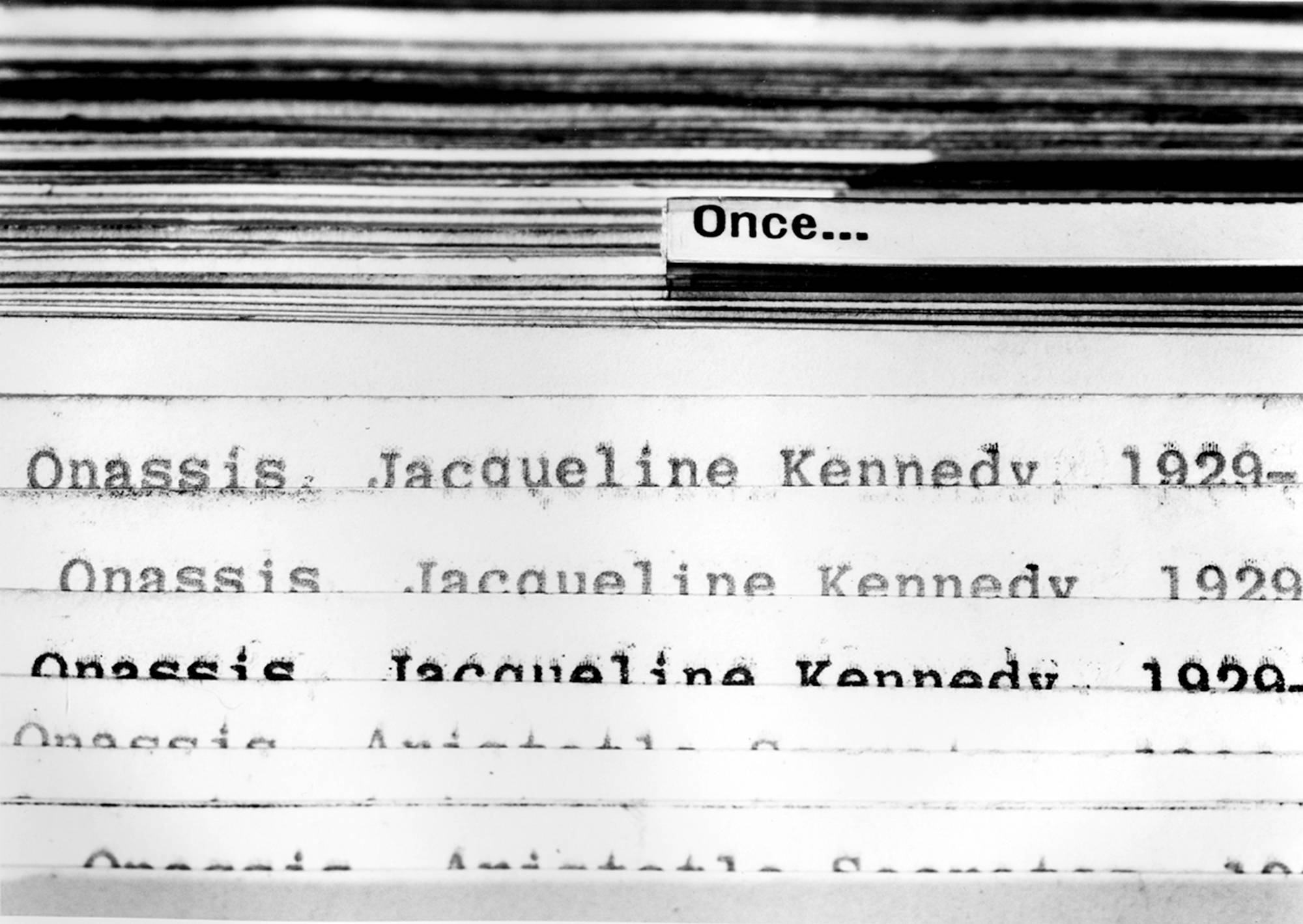 An image of a black and white photograph taken inside the files of a card catalogue from the library. There is a tab sticking up that has the word 'Once...' written on it and below, a shuffle of index cards peek out with the words Onassis, Jacqueline Kennedy, 1929-