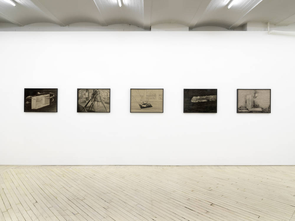 In a gallery space, a row of evenly spaced pencil drawings behind tinted glass frames. The frames are black. The drawings depict abstracted landscapes resembling constructed dream worlds.  