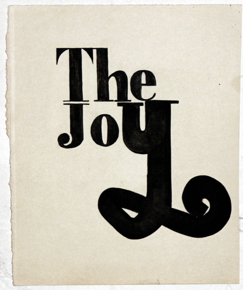 Ink drawing on paper of the words "The Joy" in a serif font, stacked on top of each other with an exaggeratedly large calligraphic "Y" against a blank white background.