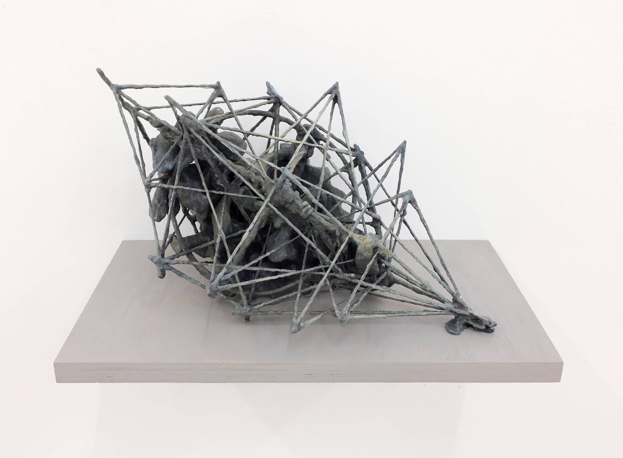 A handmade abstract sculpture resembling a kind of artifactual relic or some combination of archaic materials. The object is resting on a gray shelf attached to a white wall.