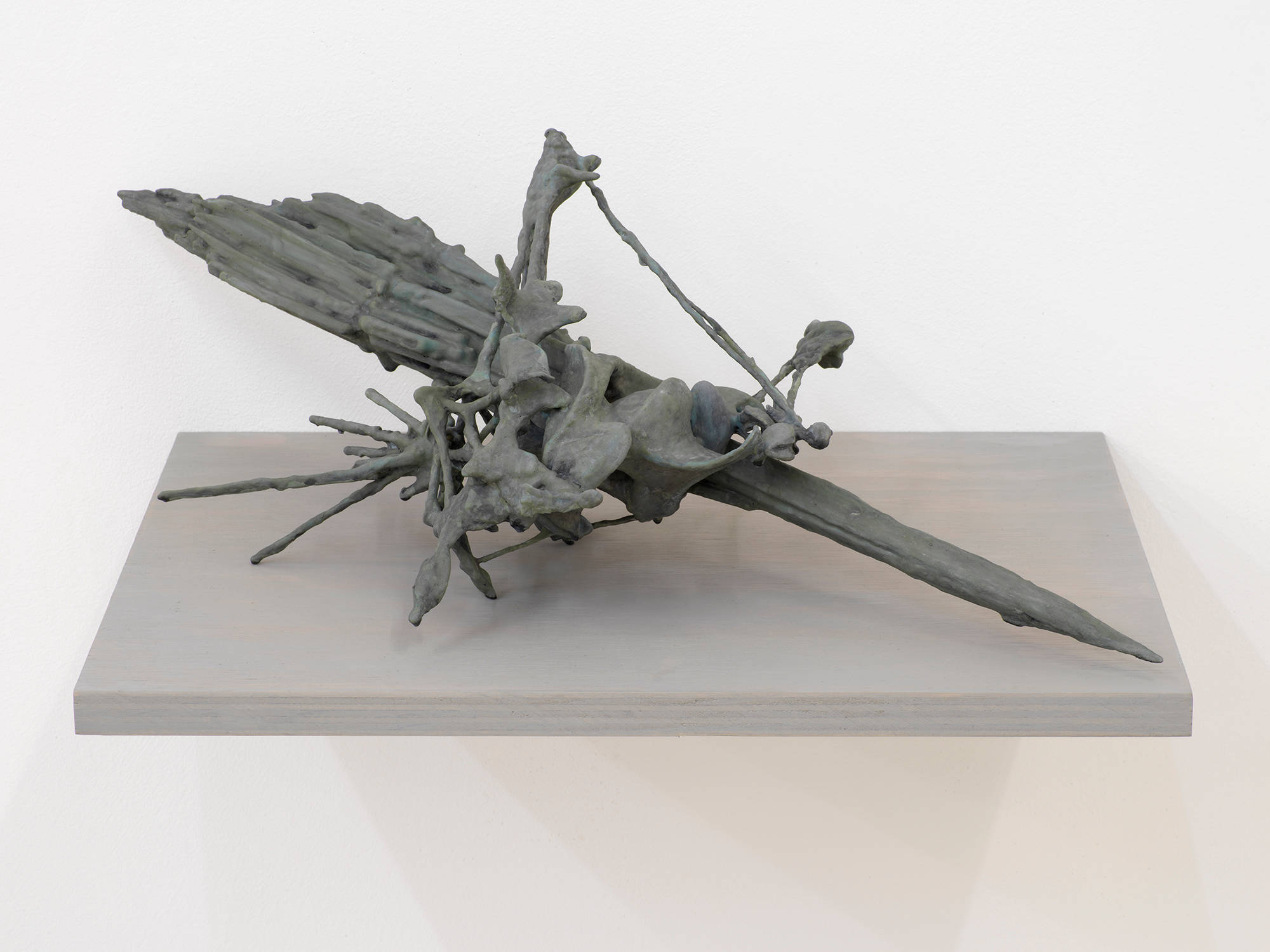 A handmade abstract sculpture resembling a kind of artifactual relic or some combination of archaic materials. The object is resting on a gray shelf attached to a white wall.