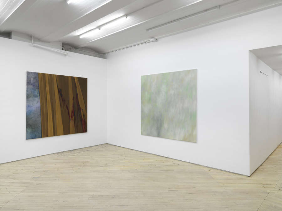 Two large, square abstract paintings are hung in the corner of a large gallery space.