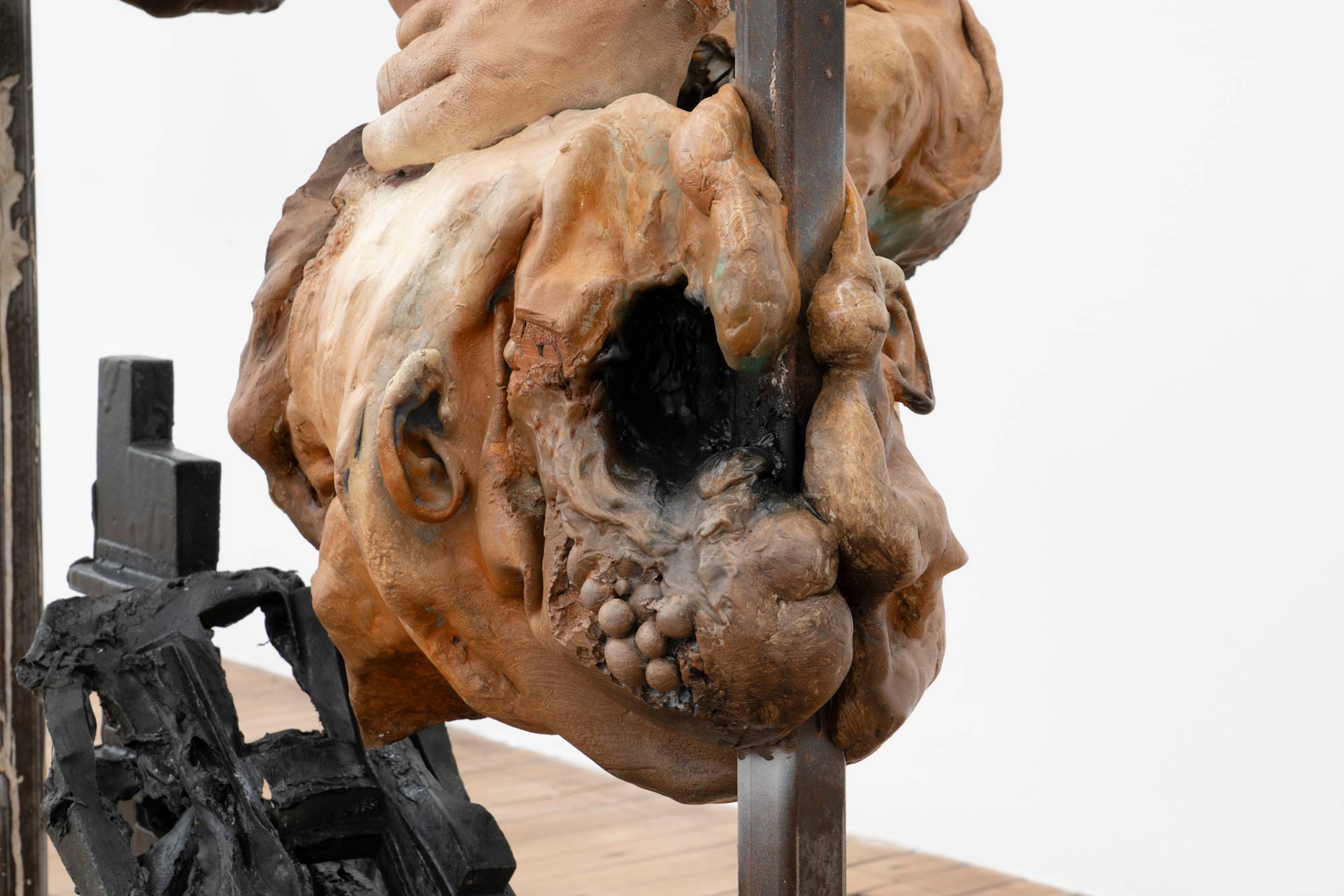 Detail of a freestanding sculpture featuring a fragmented figure, inverted and suspended from a metal frame.