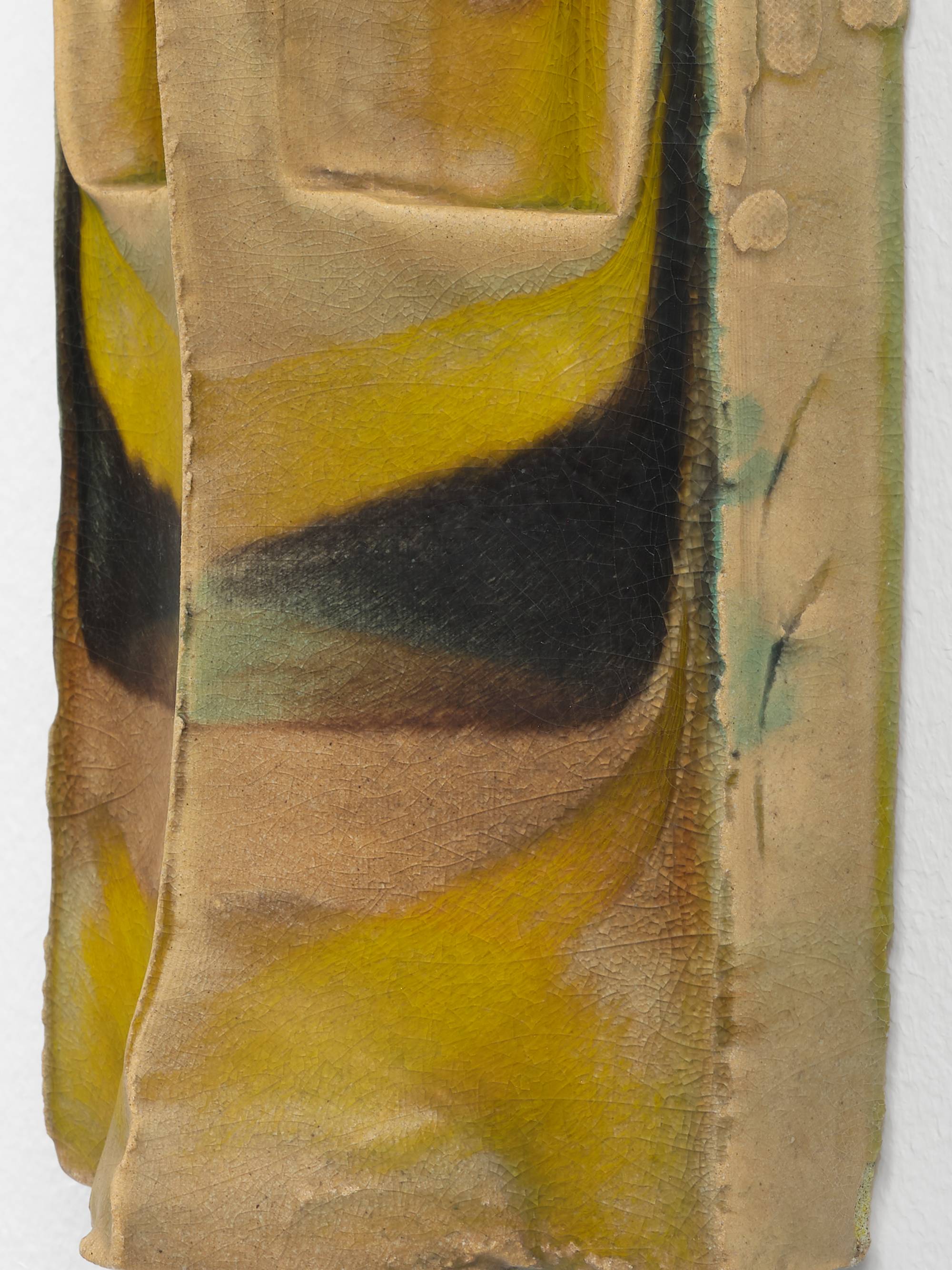Detail of a symmetrical, wall-mounted, ceramic sculpture composed of two narrow, vertical slopes that form a peak that runs parallel to the wall. In the top half of the work a shallow pocket has been carved out of each slope and the crown has been embellished with a small, curled ornament. The sculpture is glazed in hues of brown, green, and yellow.