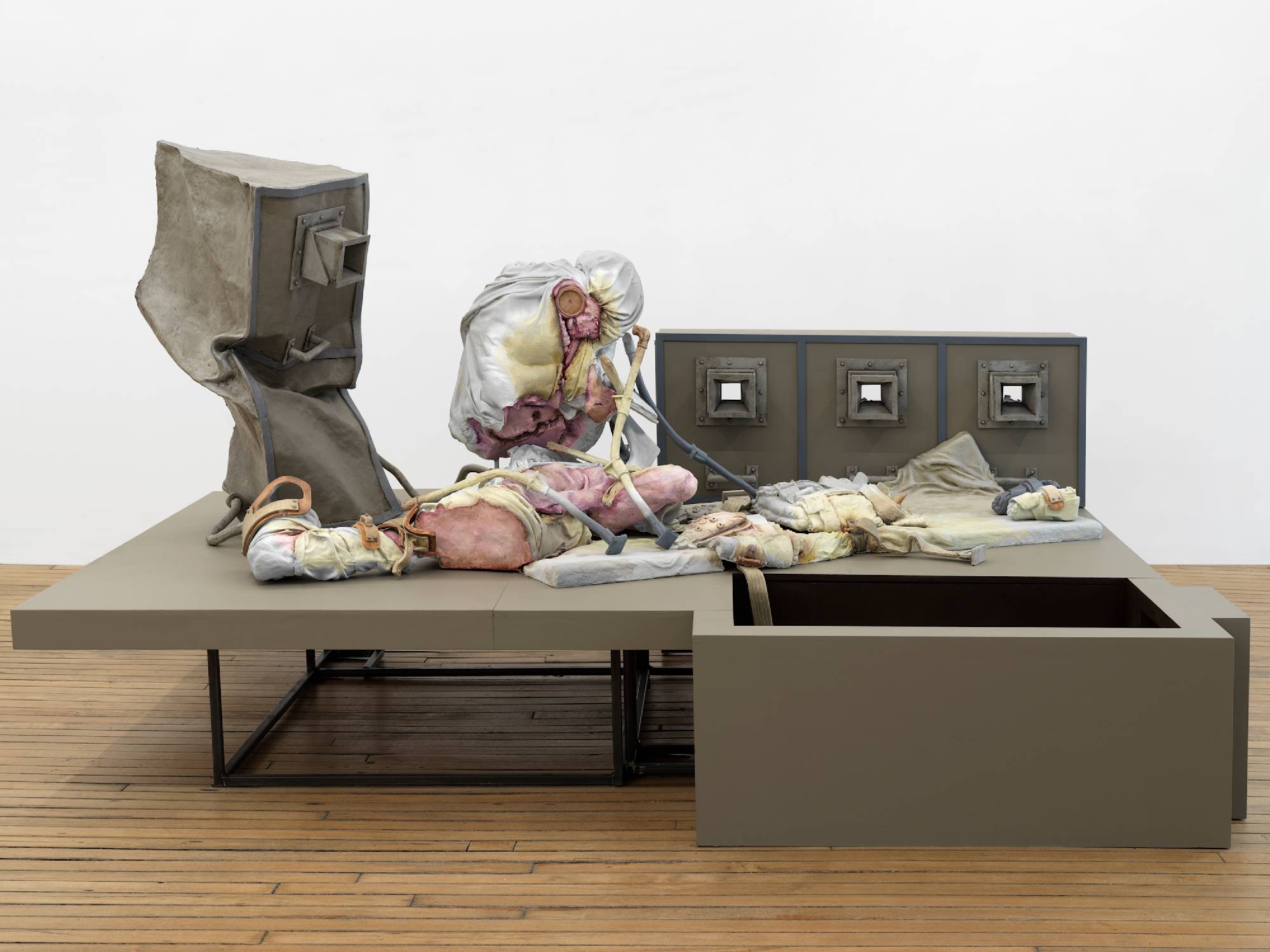 A large floor-standing sculpture depicting a combination of abstracted human forms and devices, combined with steel structures that resemble cages.