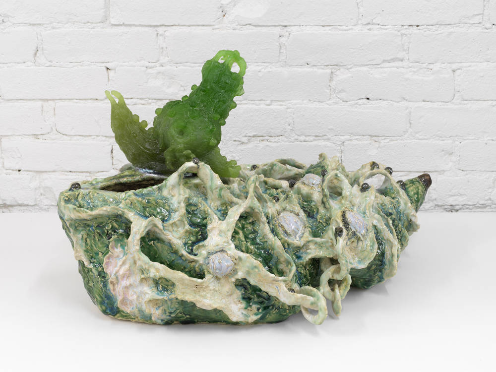 A freestanding, abstract ceramic sculpture resembling a landscape populated by different human and animal  forms.