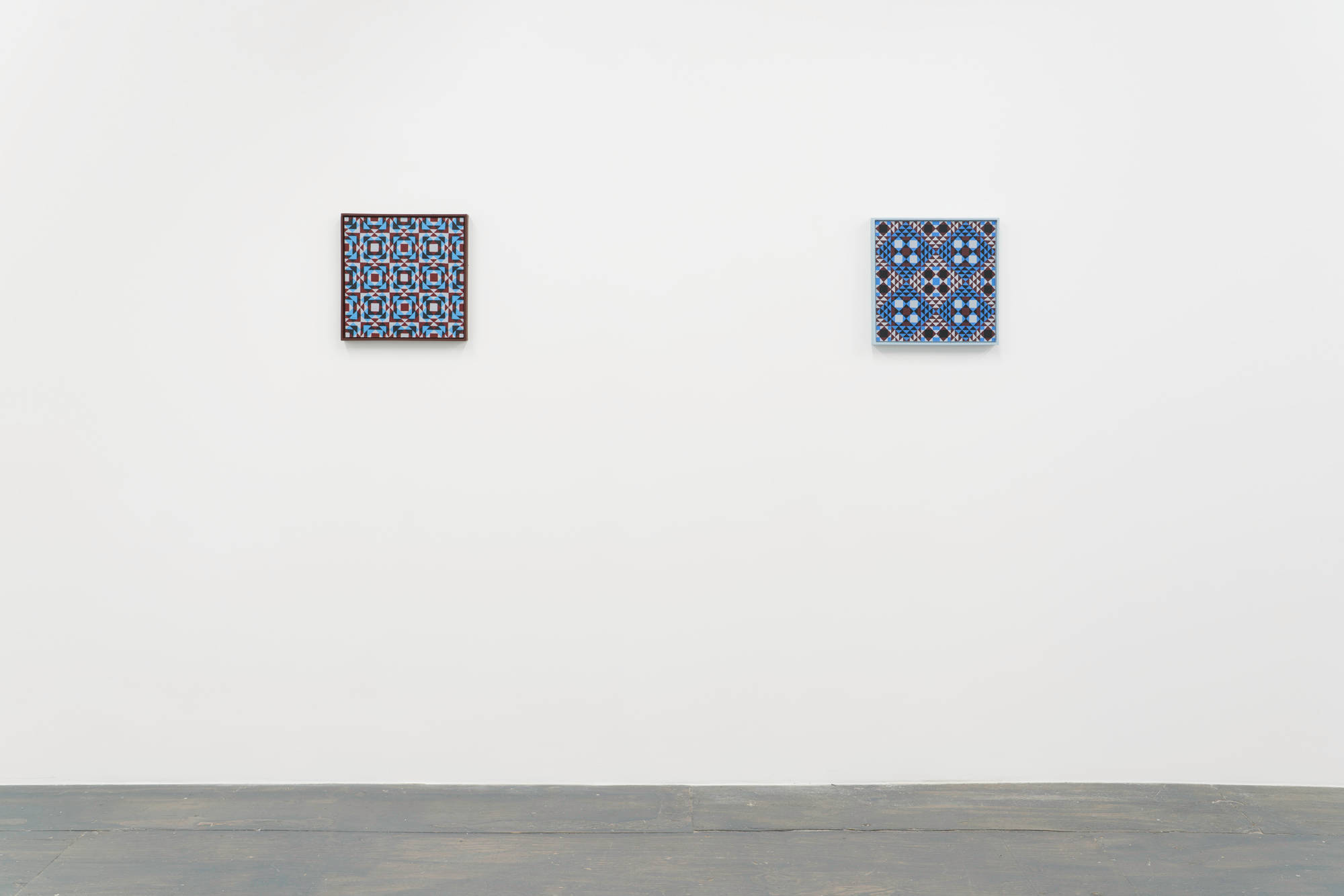 Two colorful geometric paintings consisting of a pattern of repeating diamonds and triangles hung along a gallery wall.