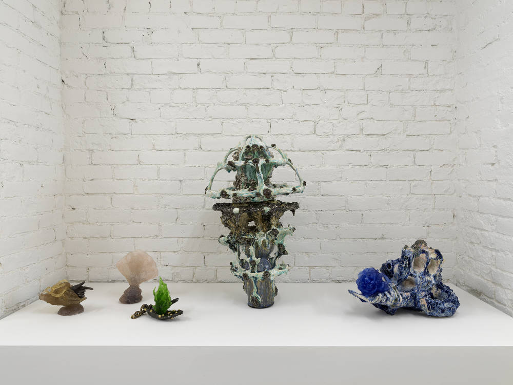 A group of abstract ceramic sculptures installed on a pedestal against a brick wall. 