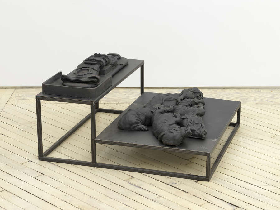 In a gallery space, an iron sculpture depicting abstracted animal forms on top of a plinth.