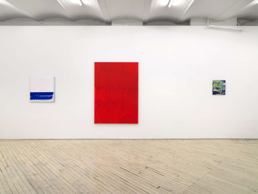 Along a long horizontal wall. A square white and blue painting, a large monochromatic red painting, and to the right a small, brushy green and purple painting. 