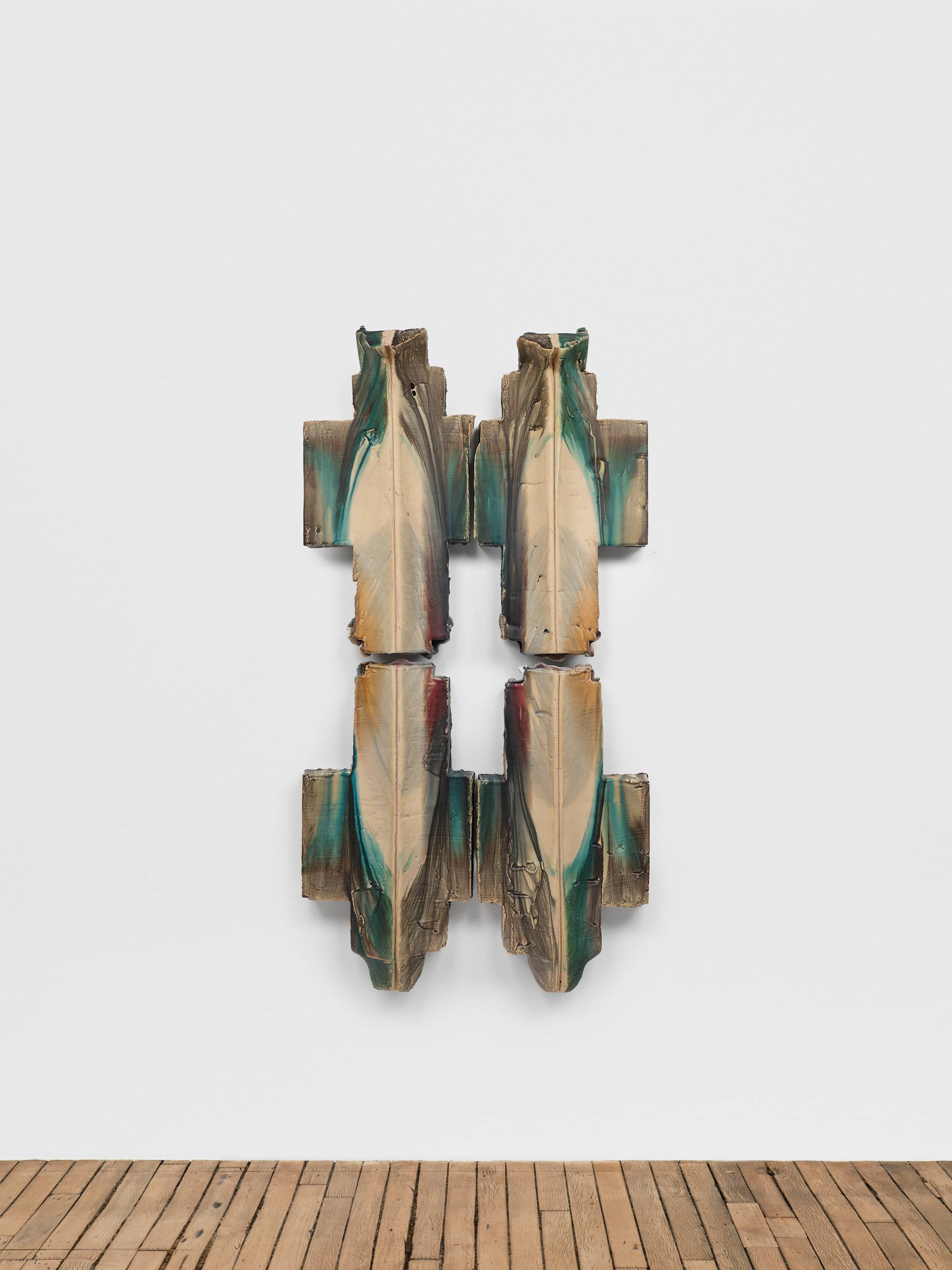 Four individual cross shaped ceramic sculptures are mounted to a white wall above a wood floor in a square orientation to form the shape of a pound sign (#). They are glazed in hues of aqua, red, and yellow.