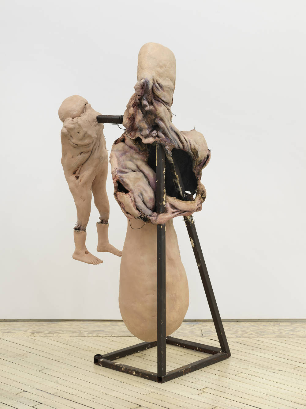 In a gallery space, an abstract sculpture resembling a human form with a steal base. 