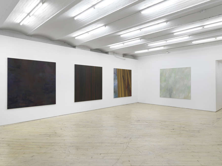 Four square, large abstract paintings hung evenly spaced throughout a large gallery space.