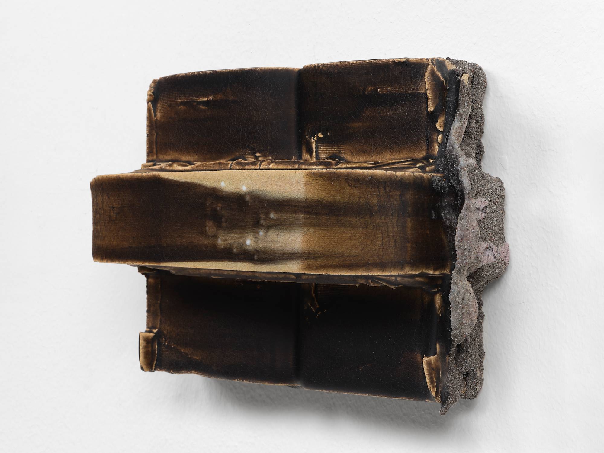 Three quarter view of a small, brown, ceramic sculpture featuring two vertical cuboids with a long horizontal band stretching the full width embedded with a circle of white beads.