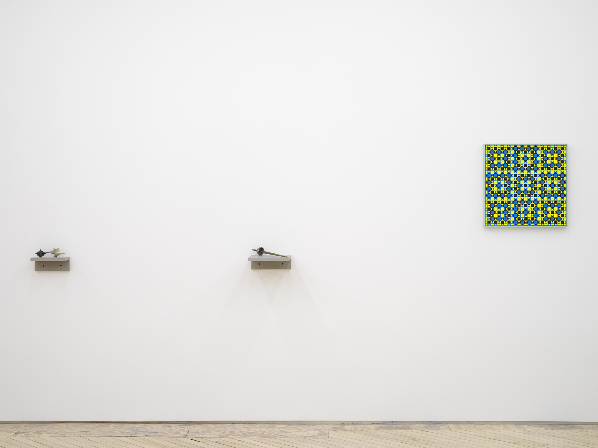 On a long white wall, two small handmade sculptures resembling bones or other organic matter. The sculptures are hung on small gray shelves. To the right is a painting depicting a grid of crisscrossing lines generating many rectangles, and triangles. The dominant colors are hues of greens and blacks. 
