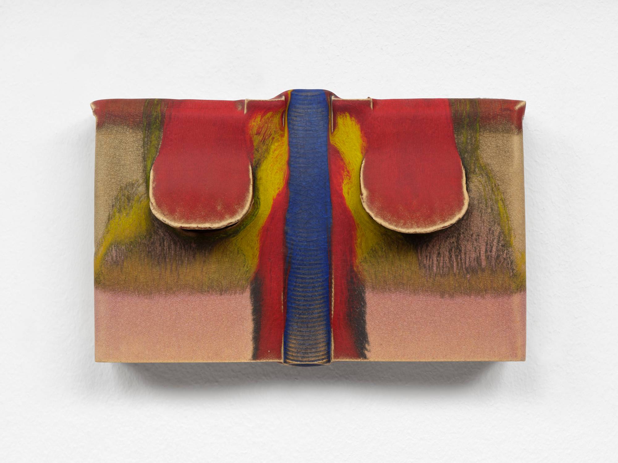 A small, rectangular, ceramic sculpture, with two red glazed flaps lifting on either side of a vertical blue glazed trough. Streams of Pink and yellow glaze fill the rest of the composition.