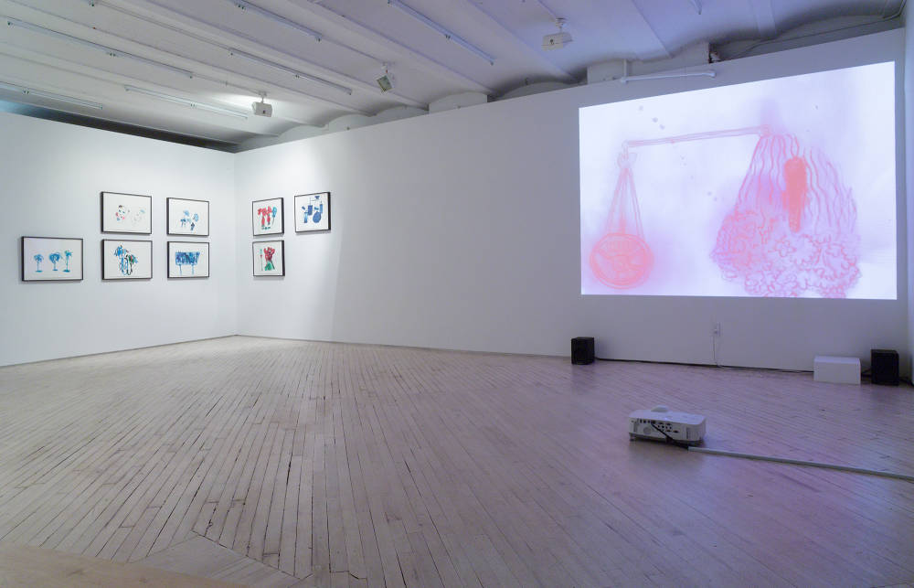 In a darkened gallery space, to the right a projector rests on the floor projecting an abstracted image of pink and purple forms onto a wall. To the left of the room is a suite of spotlit black frames containing drawings of various colors. The frames are staggered in twos in the corner of the room. 