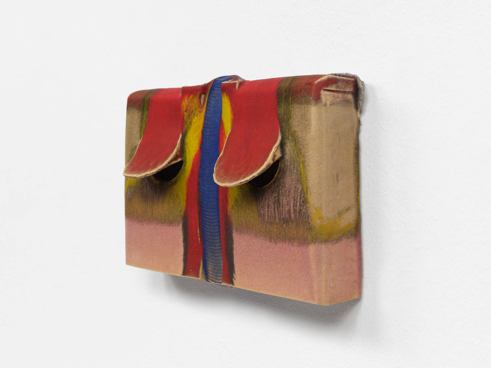 Three quarter view of a small, rectangular, ceramic sculpture, with two red glazed flaps lifting on either side of a vertical blue glazed trough. Streams of Pink and yellow glaze fill the rest of the composition.