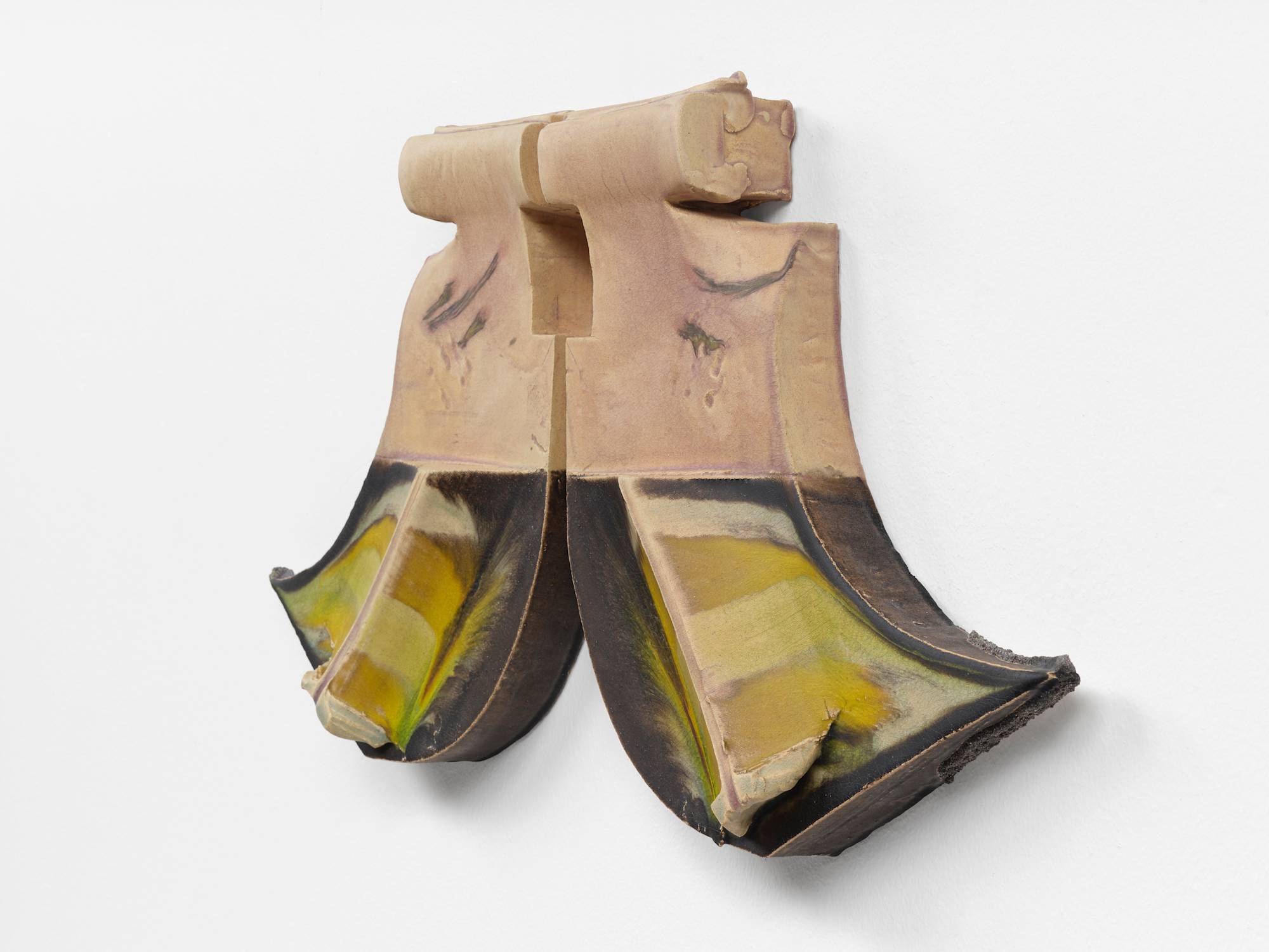 Three quarter view of two ceramic sculptures hanging on a wall mirroring each other. The two pieces resemble the letter "J", one forwards, one backwards. A spine runs diagonally down each bottom swoop, striped with yellow and green glaze, against a background of dark brown glaze.