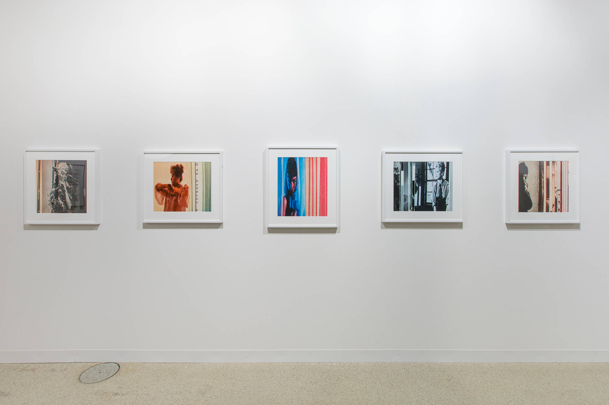 A straight on shot of a white wall featuring 5 color photographs framed and matted in white. Each shows the fanned out pages of books, with a female figure, an illustration from within the book captured between the pages.