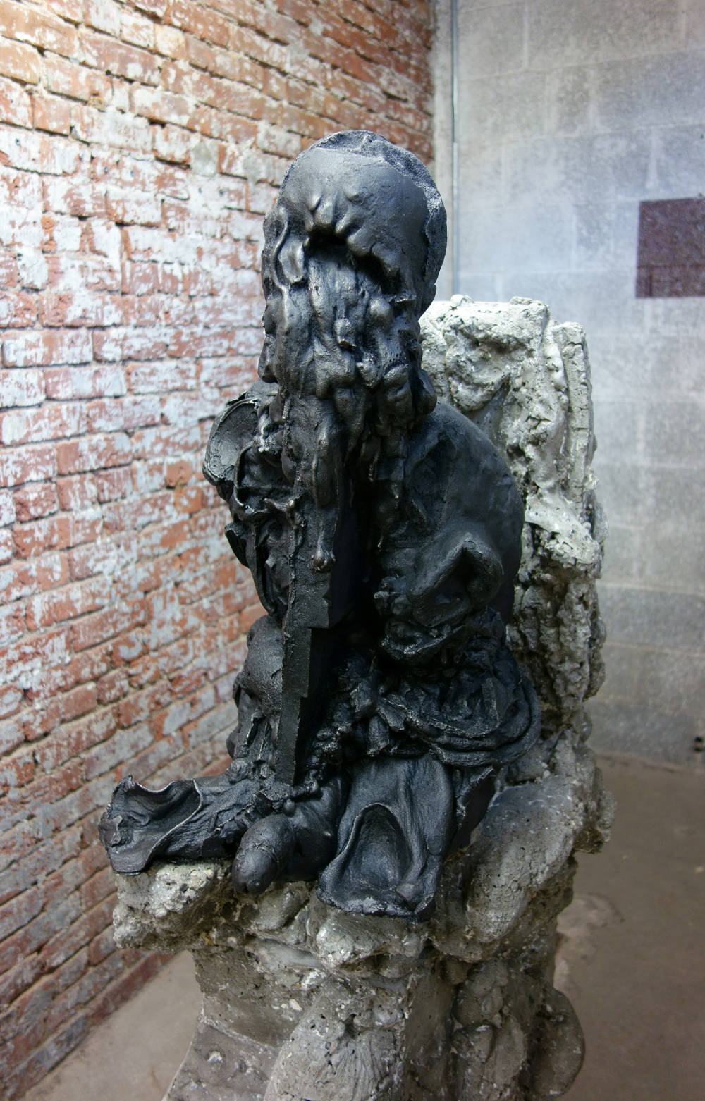 Installation view of metal and concrete sculpture, depicting a cast iron sculpture of a head and torso melting and/or decaying.