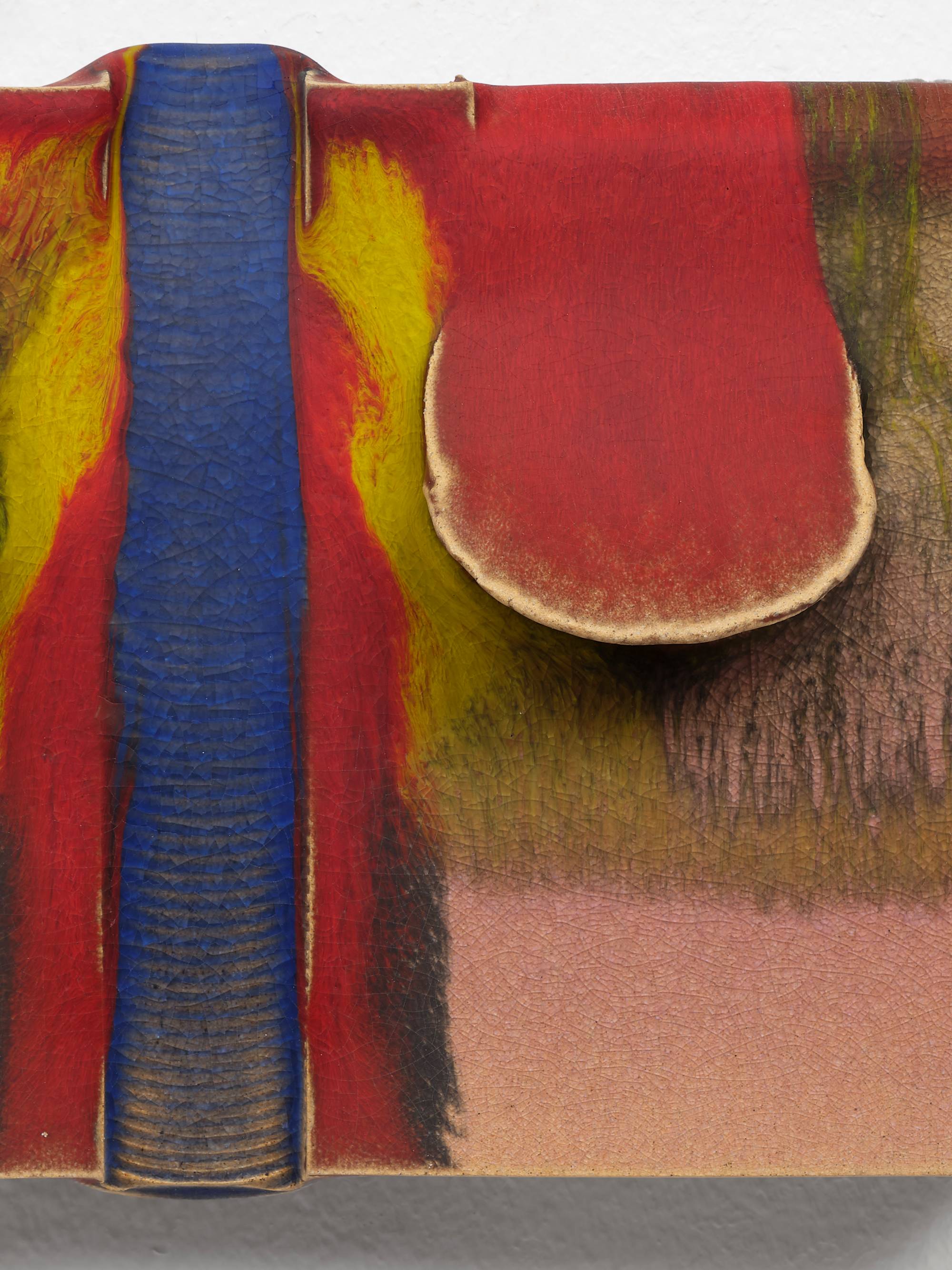 Detail of a small, rectangular, ceramic sculpture, with two red glazed flaps lifting on either side of a vertical blue glazed trough. Streams of Pink and yellow glaze fill the rest of the composition.