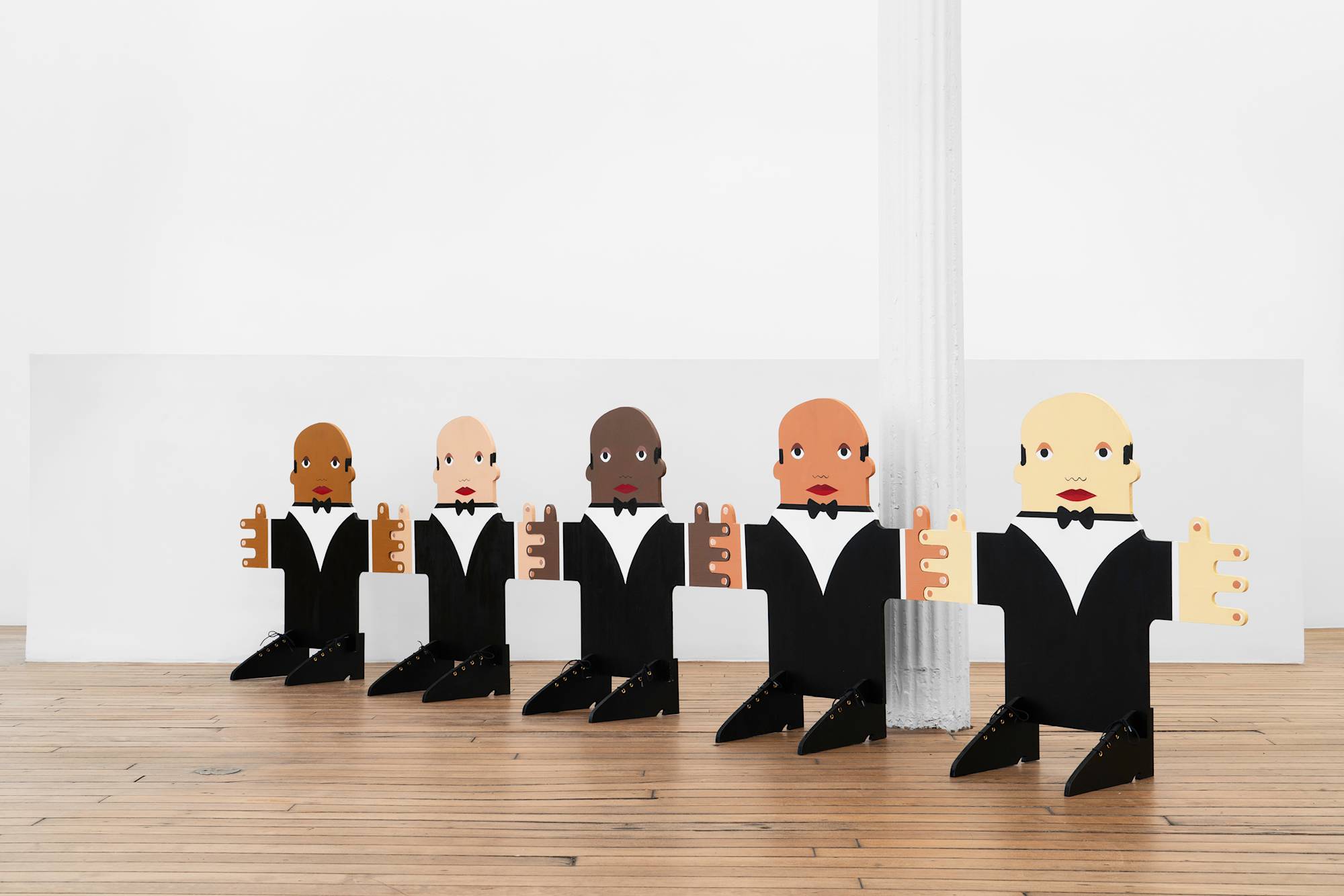 A sculpture depicting five waiters of different ethnicities interlocking their fingers to form a straight light. They are constructed of MDF and painted to wear matching tuxedos. Shoes are slotted into their body frames perpendicularly to stabilize the structure.