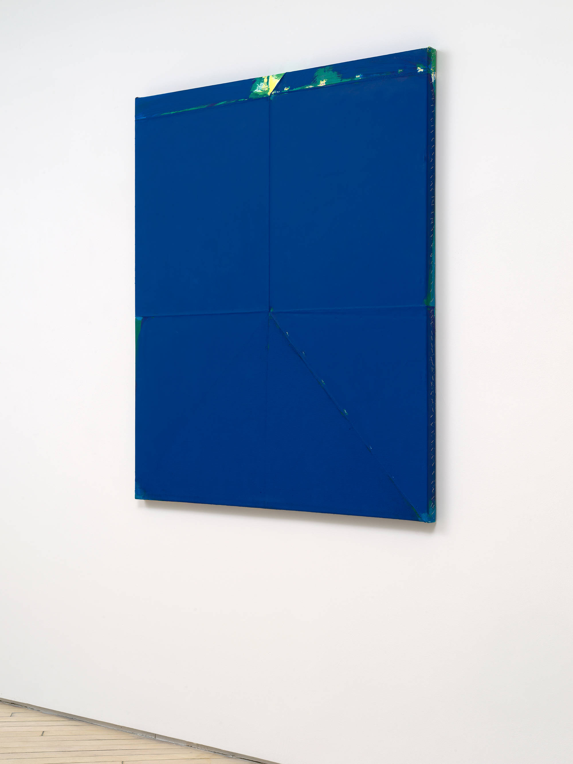 A sideview of a large blue monochromatic painting with a green accent at the top.