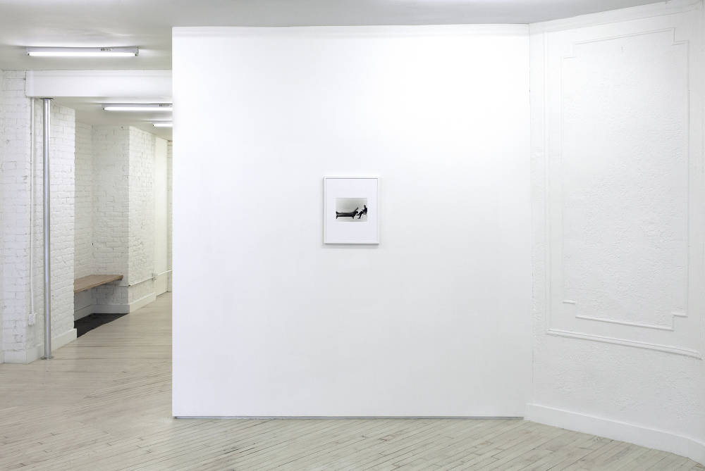 View of the front room of Bureau - white walls and off-white wood floors. The front facing wall has a small black and white photograph hanging on it at center.
